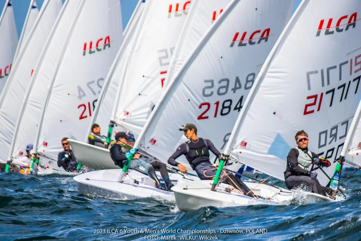 A tightly packed line of ILCA dinghies racing upwind, sailors hiking